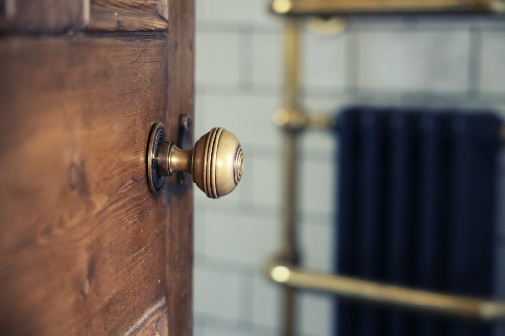 A brass door handle on an old wooden bathroom door.