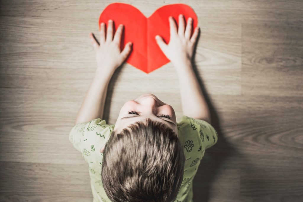 A boy with his hands pressed down on a cutout paper red heart.