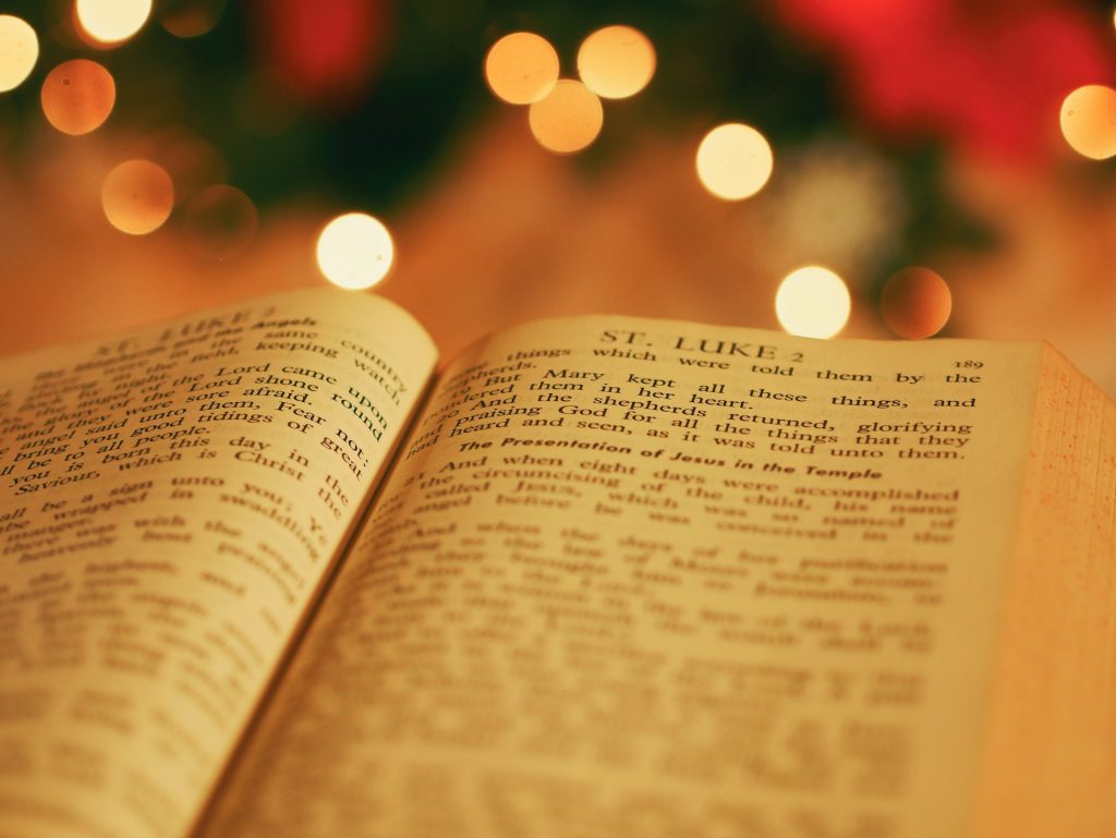 A close up of a Bible open on the page of Luke Chapter 2 with warm Christmas lights in the background.