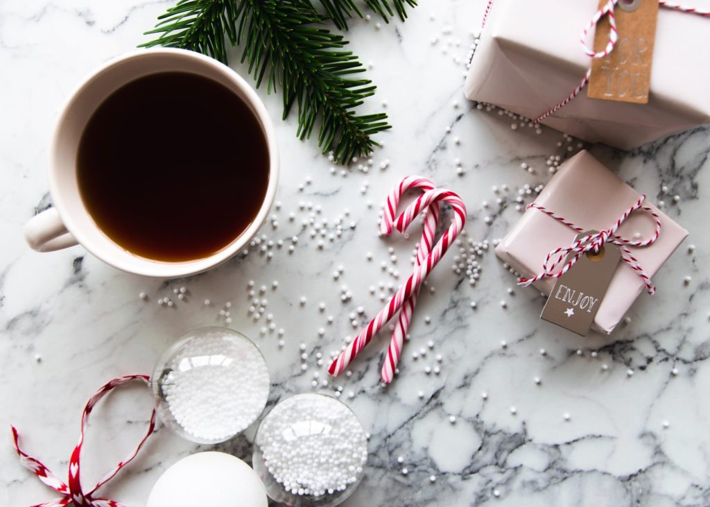 A coffee mug, candy canes, Christmas tree branch, presents, and small white balls sitting on a marble top.