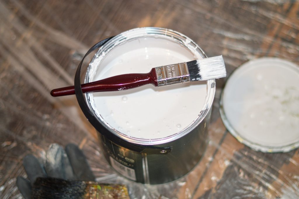 A paintbrush lying across an open tin of paint.