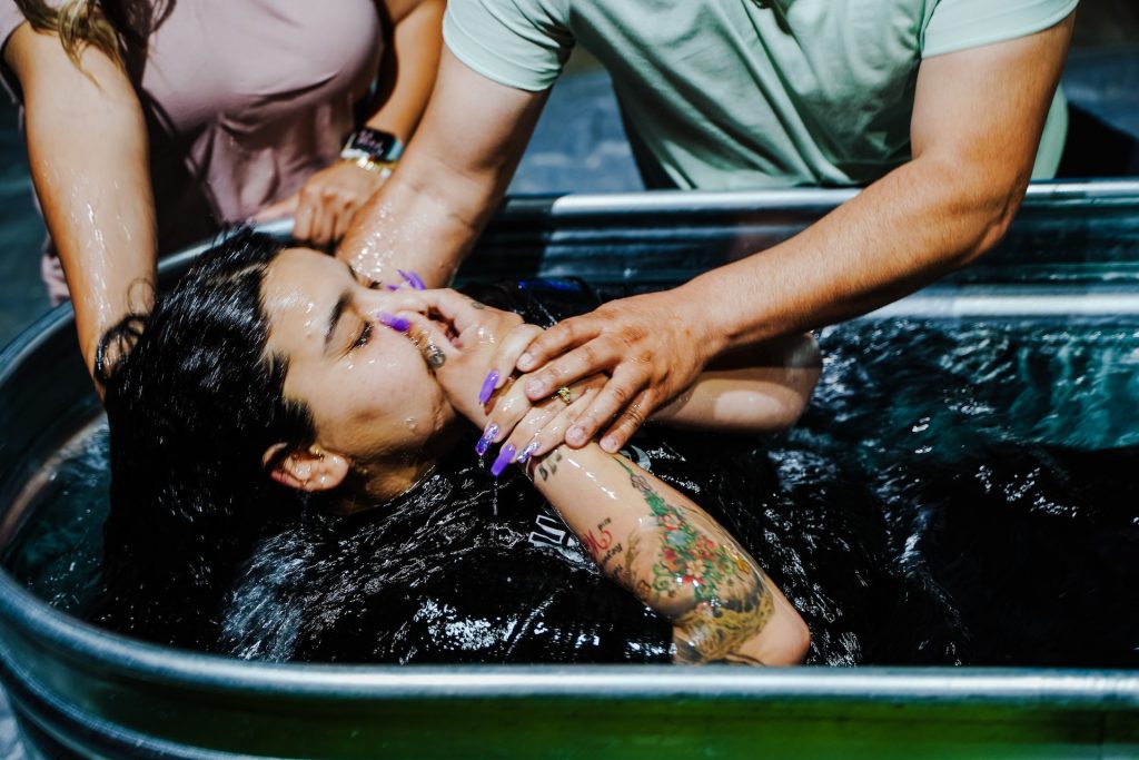 A girl with her fingers on her nose being held as she is plunged backwards into water in a tin bath.