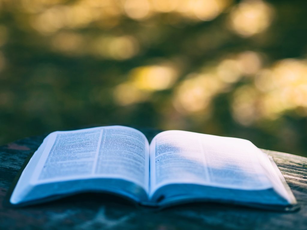 An open Bible lying on a wooden bench.