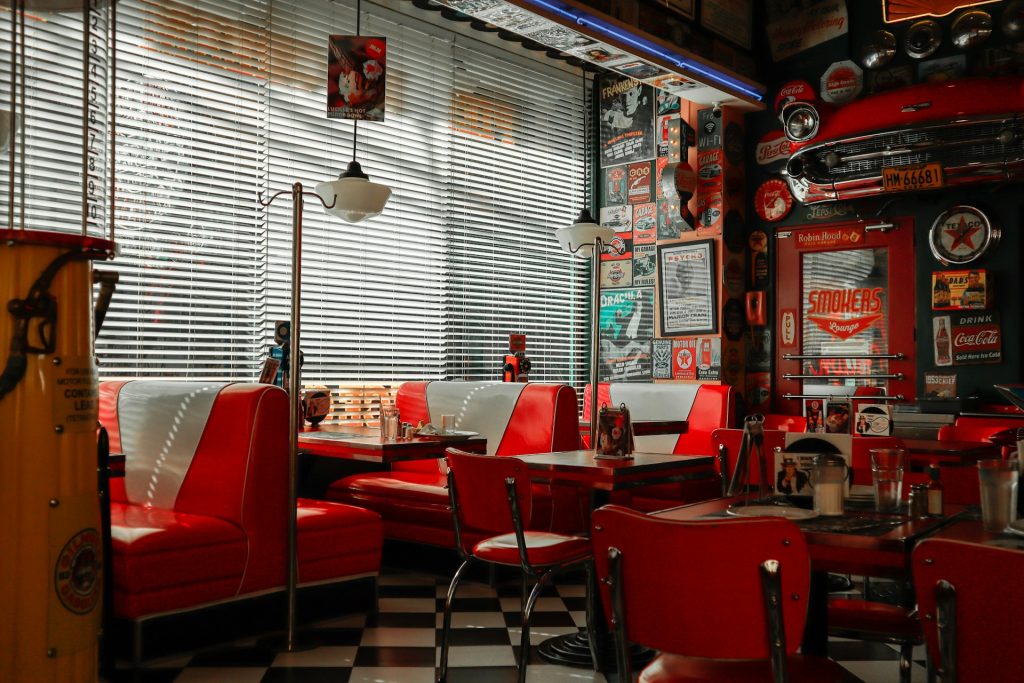 The inside of a 1950s retro diner with cool posters on the walls, fenders, number plates, and booths.