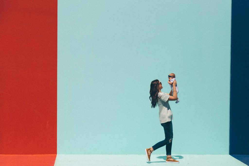 A woman walking along a street and holding up a baby.