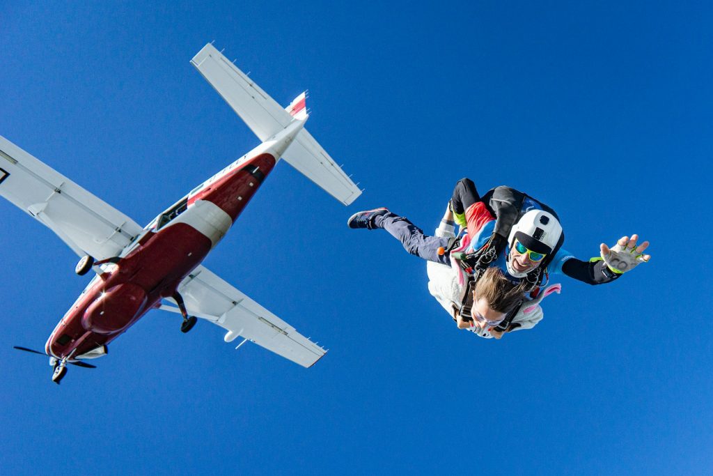 A man and woman skydiving out of an airplane, smiling and waving.