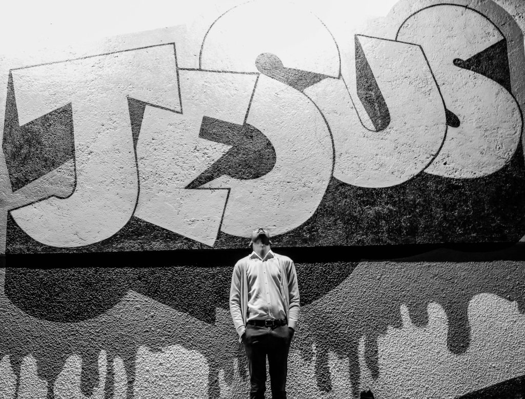 A man looking up a a huge piece of graffiti of the word Jesus.