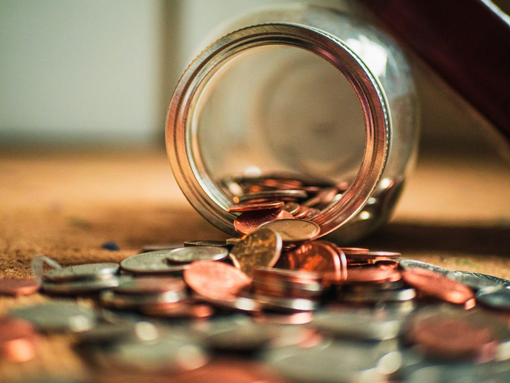 An upturned jar with coins spilling out of it.