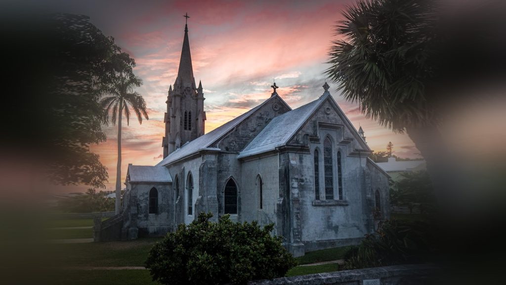 A stone parish church at sunset surrounded by palm trees.