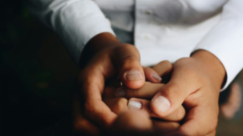 The close-up of hands wrapped around the hands of another in a caring way.