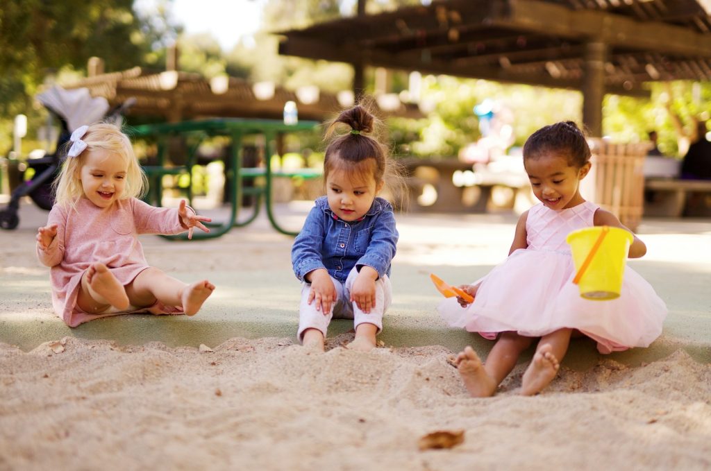 Three little girls sitting and playing in a sandpit.