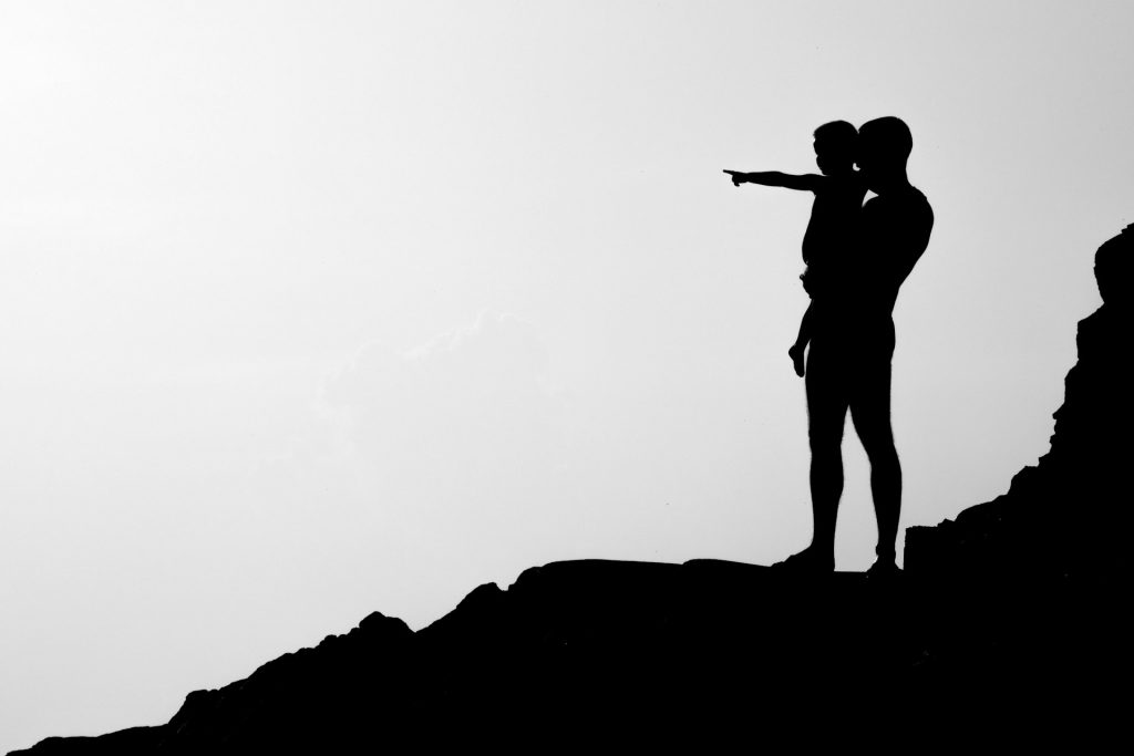 The silhouette of man holding a child who is pointing into the distance.