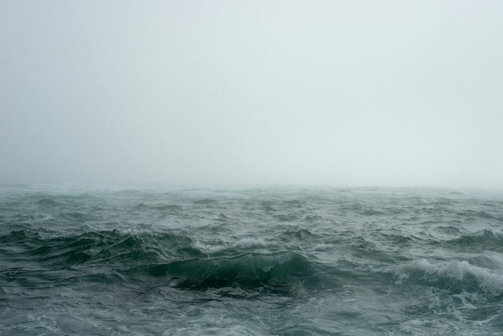 A rough and stormy sea with a cloudy rainy fog above it.