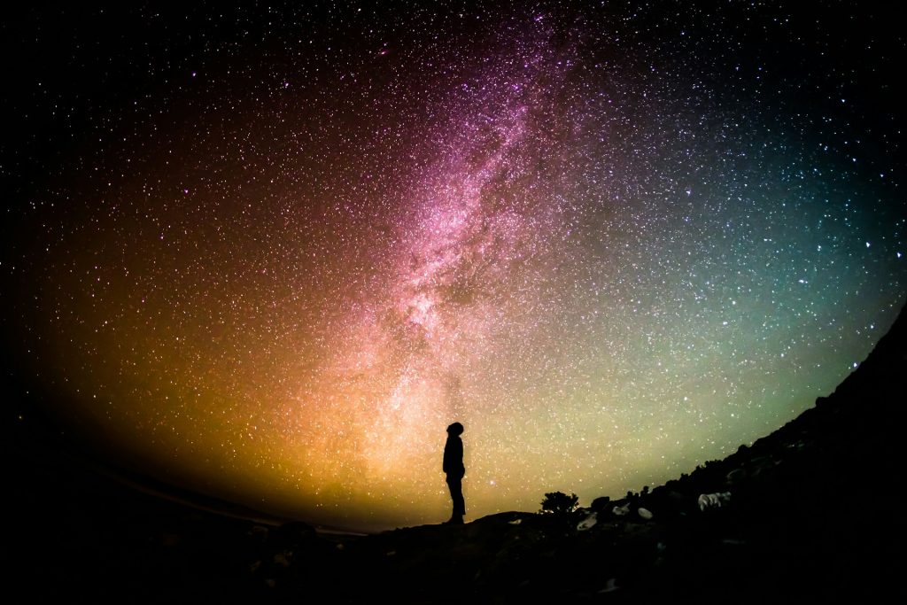 A man staring up at the night sky with a plethora of stars overhead.