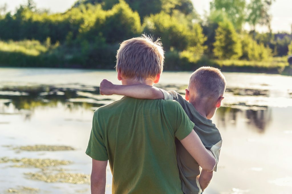 Two boys with their arms around each other, viewed from the back.