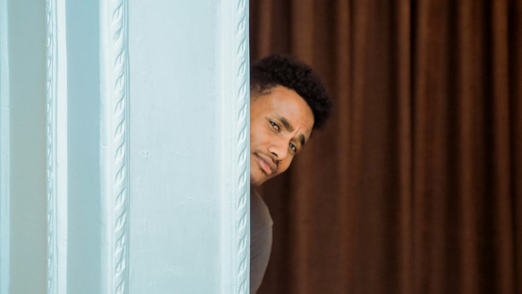 A man pokes his head from behind a screen with raised eyebrows as if to ask a question.