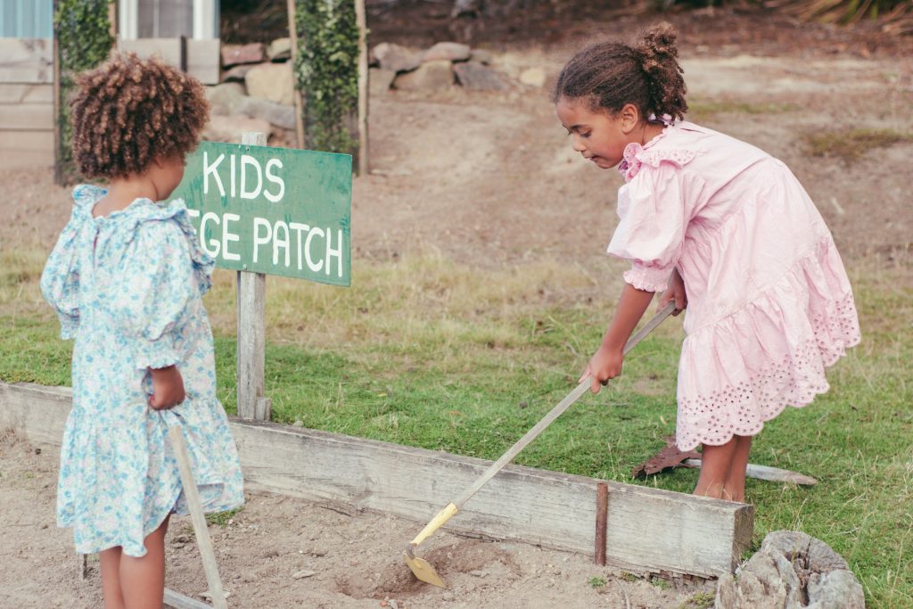 Two small children playing with spades in dry soil.