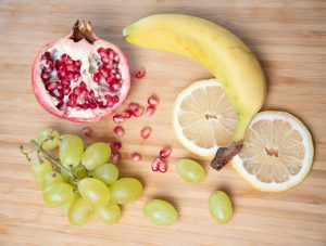 A selection of fruits - whole and halved - including pomegranate, lemon, grapes, and a banana.