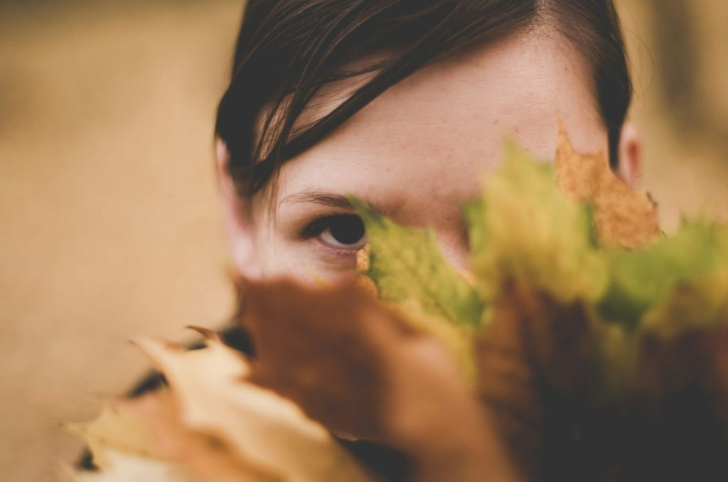 A girl hides behind a tree and you can just see her eyes poking out from behind the autumnal maple leaves.