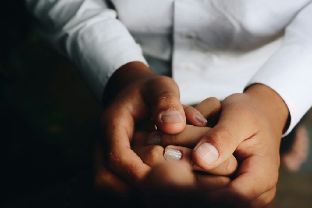 A close-up of two people hold hands comfortingly. One pair of hands enclosing another.