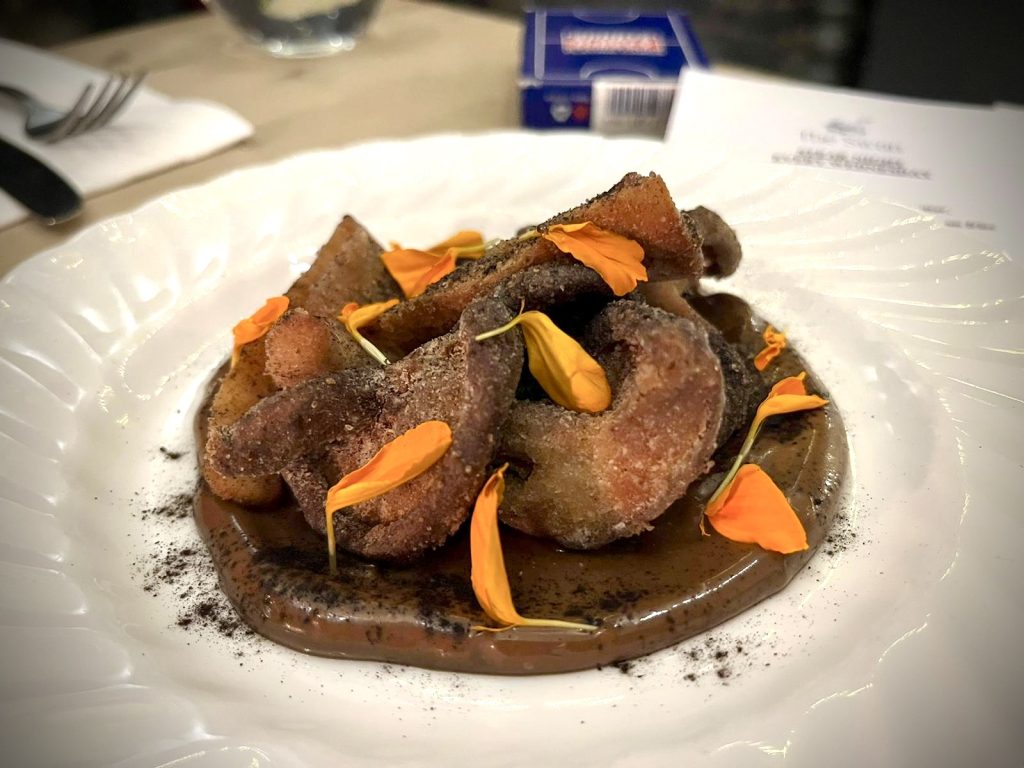 A plate of fried mushrooms on a bed of black garlic mayonnaise adorned with orange petals.