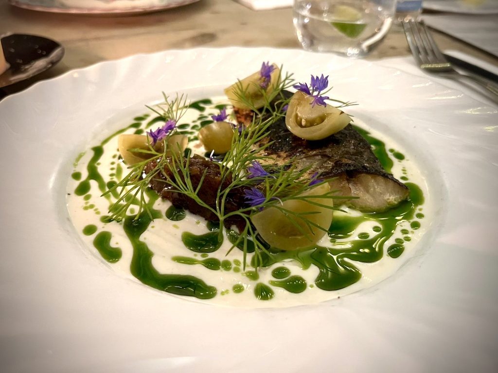 A fine mackerel starter on a plate with a fillet of mackerel, fennel, green tomatoes, and a green jus.