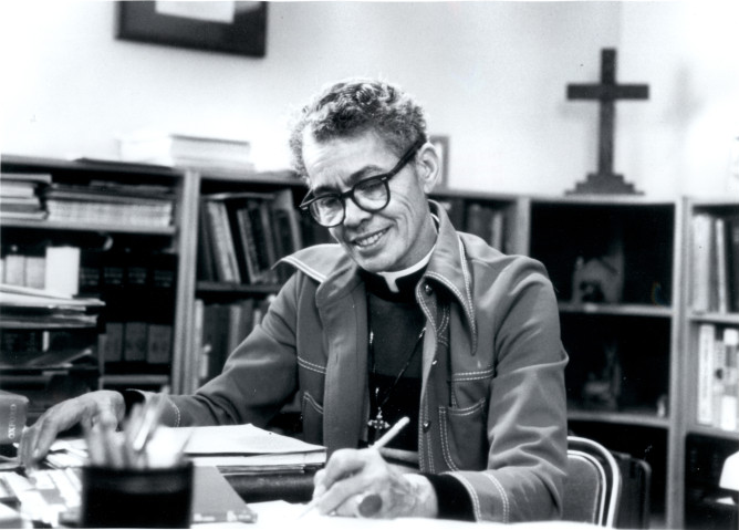 A portrait photograph of Pauli Murray seated at a desk with pen in her hand. University of North Carolina at Chapel Hill