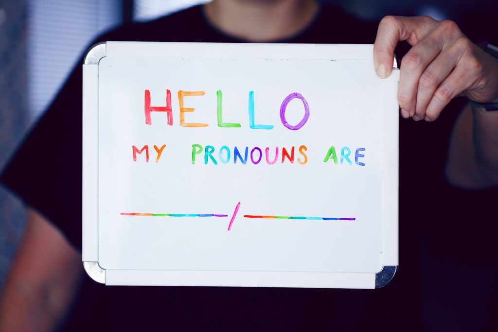 A person holds up a sign with multicoloured lettering spelling out: My pronouns are blank and blank.