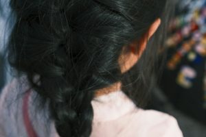 The back of a young girls head, her thick, black, bundled hair falling down her back.