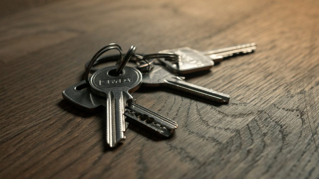 A bunch of silver house keys sitting on a wooden table top.