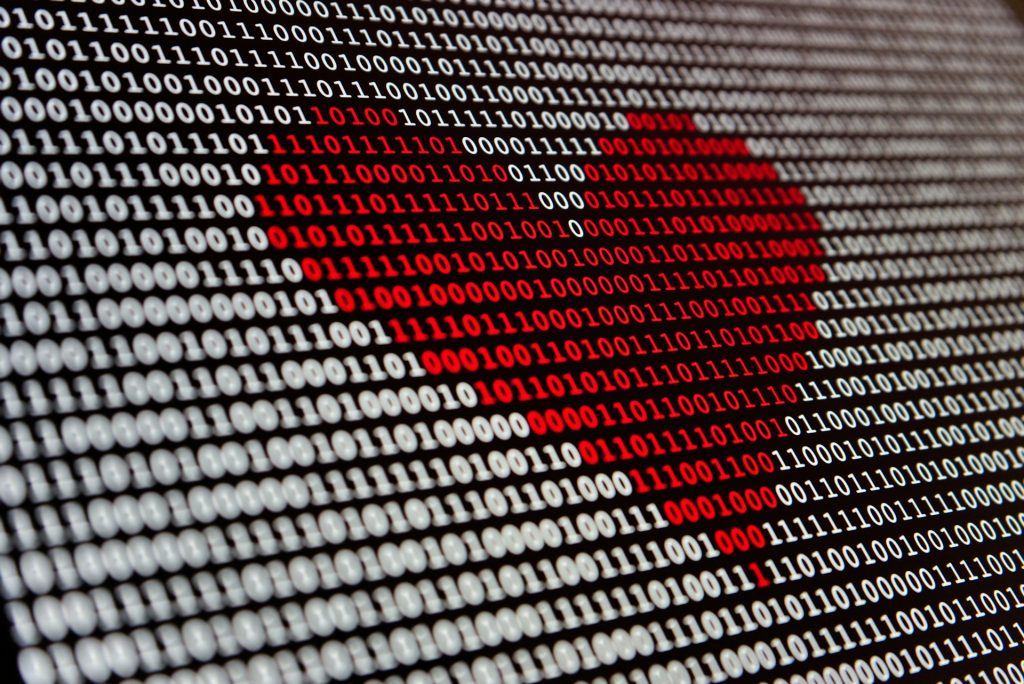 A screen is filled with white binary numbers - zeros and ones. Some of them are red and make the picture of a heart.