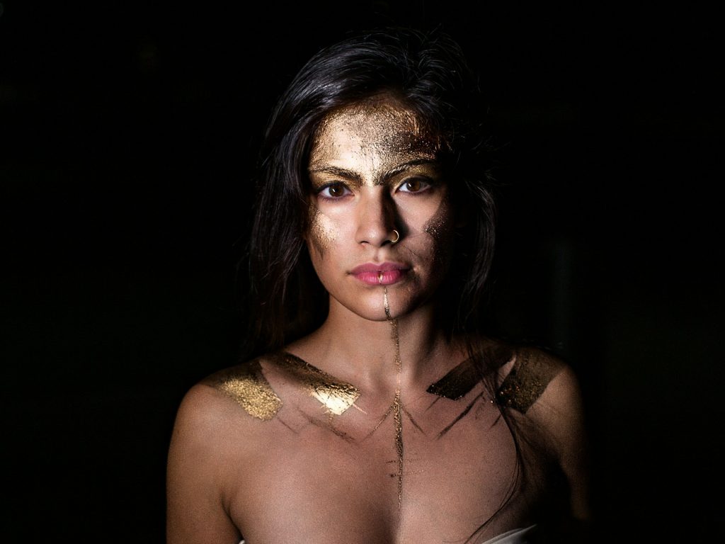 A woman stands, with warrior paint, defiant and determined, exuding power and confidence.