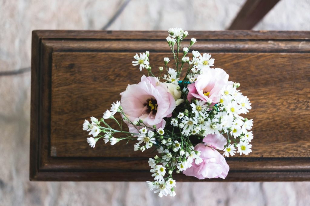 The end of a wooden coffin viewed from above with a bunch of pink and white flowers placed on top if it.
