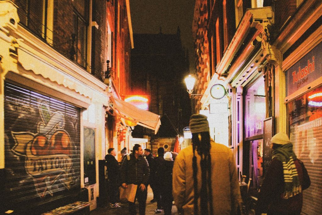 People walking down an urban city street at night illuminated by the street lights.