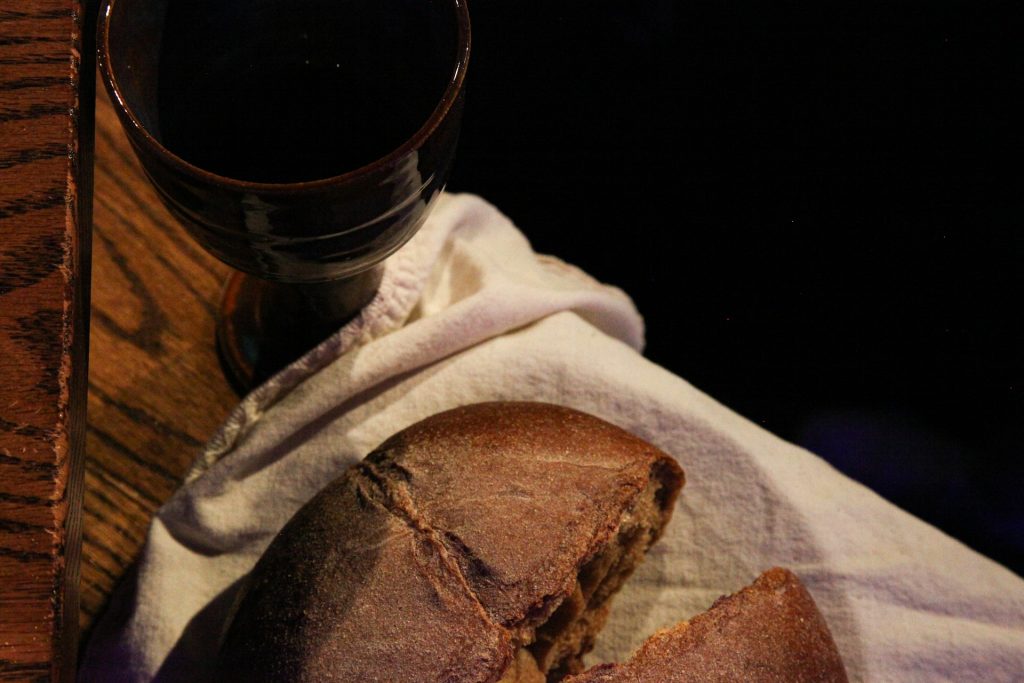 A loaf of bread and goblet of wine sit on a wooden table.