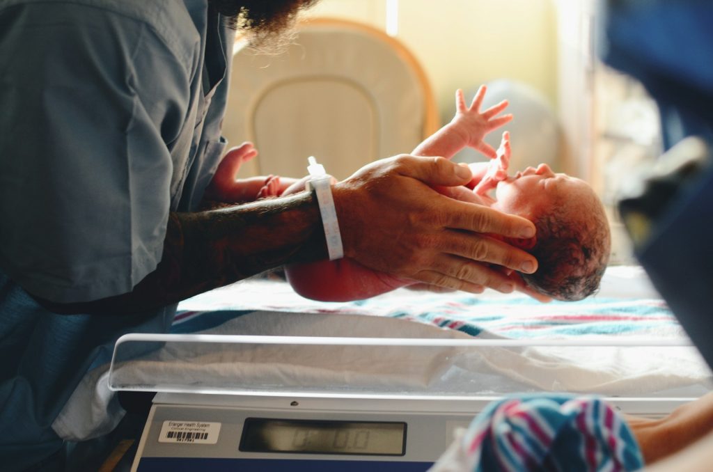 A newborn baby is being placed on weighing scales by a midwife or doctor.