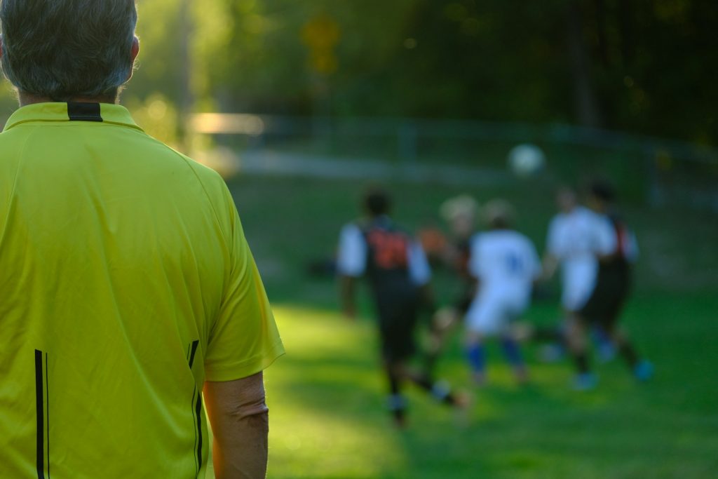 A man, probably a coach, looking at a group of footballers on a field.