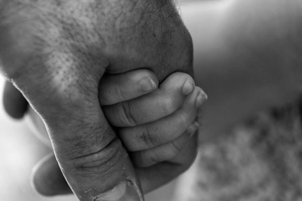 An adult mans hand holds gently a child's hand.