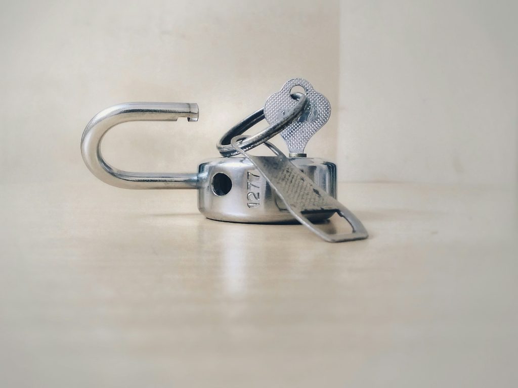 A silver padlock lies open and on its side with the key in it. Photo by Basil James on Unsplash.