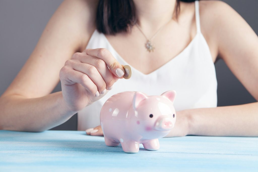 Giving A woman drops a single coin into a piggy bank.
