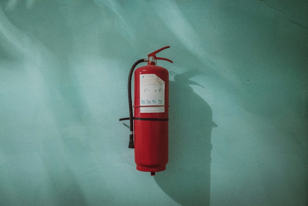 A red fire extinguisher sits attached to a wall painted a green/blue.