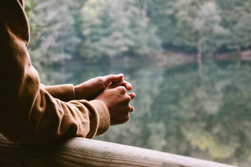 A man rests his arms on a wooden balcony overlooking a still lake communicating aloneness and contemplation.