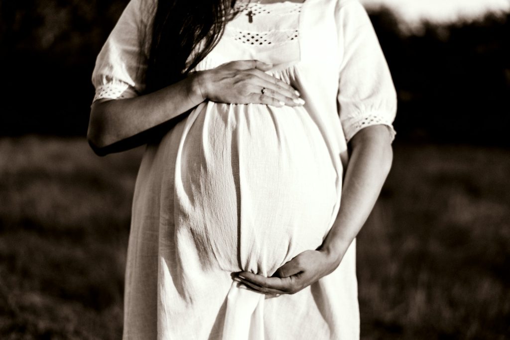 A woman in a white dress holds her pregnant 'bump'.