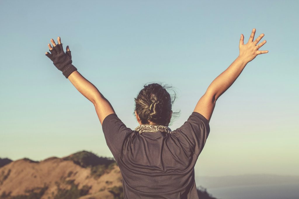 Both A woman stands on a mountain top raising her hands in exultation.