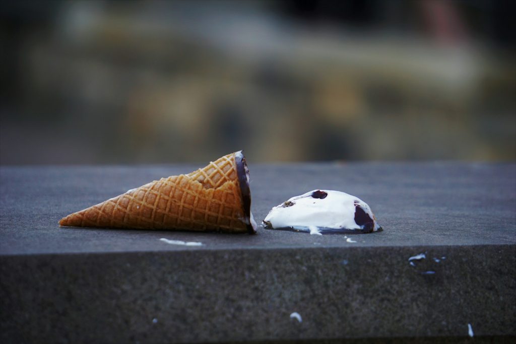 An ice-cream cone lays on a wall with the ice-cream splatted out. Broken.
