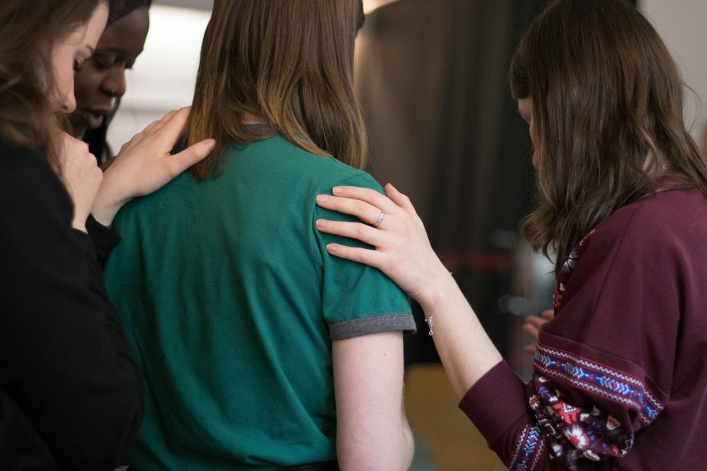 A group of women gather and lay hands on a woman and pray for her.