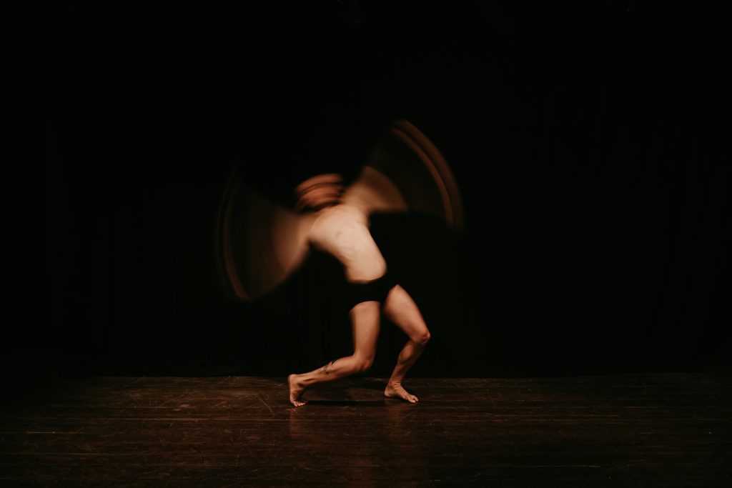 A person waves their arms and bends their body, clad only in an undergarment, as they dance.