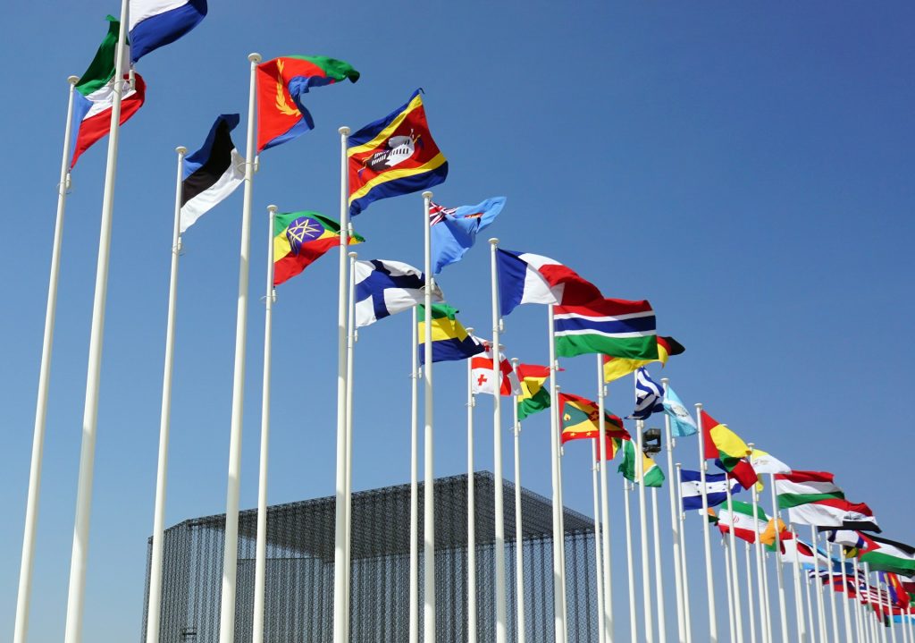 Two rows of white flag poles outside the United Nations with the flags of different countries blowing in the wind.